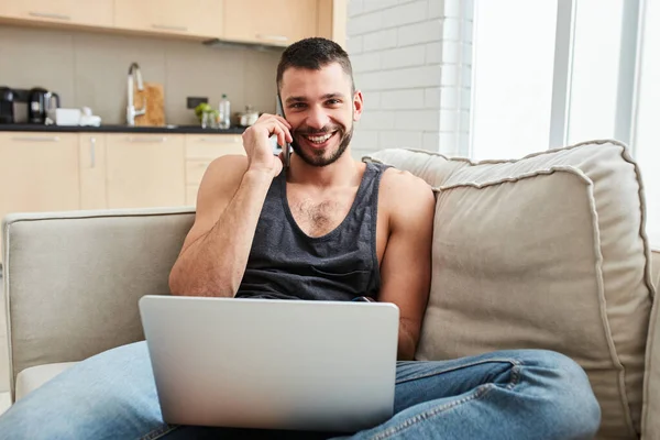 Joven alegre hablando por celular y usando laptop — Foto de Stock