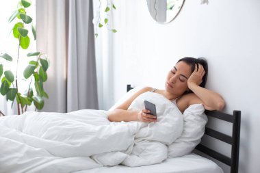 Genç bir kadın akıllı telefonuyla tembel bir sabah geçiriyor.