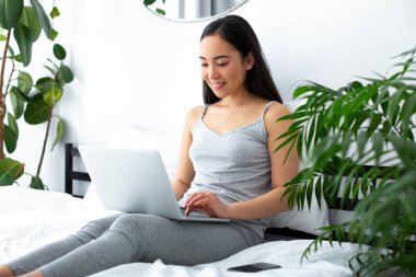 Yatak odasında modern teknolojileri kullanan neşeli genç bir kadın.