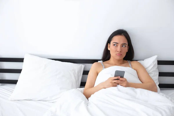 Funny young lady sitting with cell phone in bed — Stock fotografie