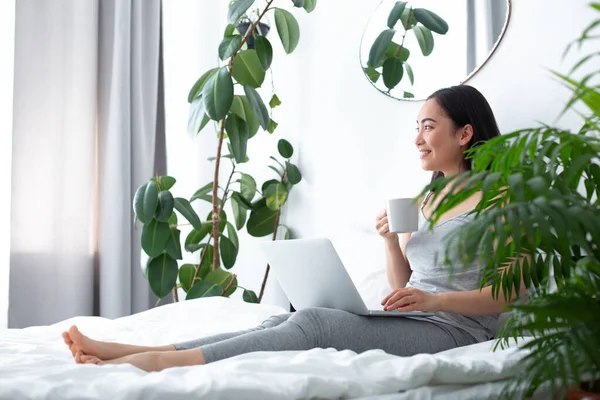 Mujer feliz con portátil bebiendo café de la mañana en la cama —  Fotos de Stock