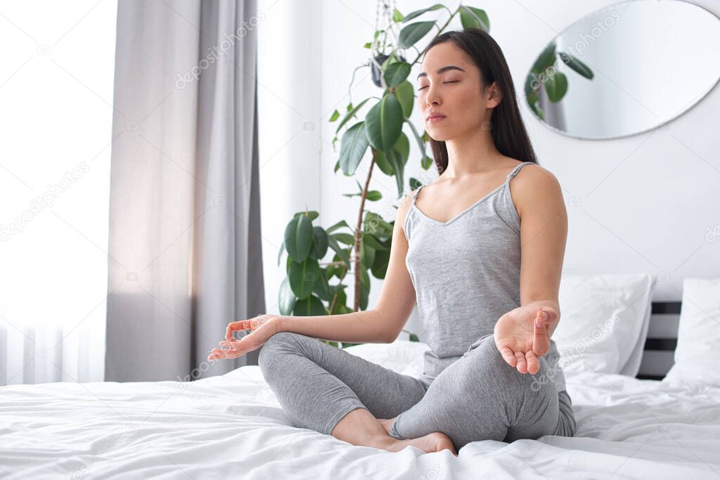 Calm young woman doing mental practice on bed