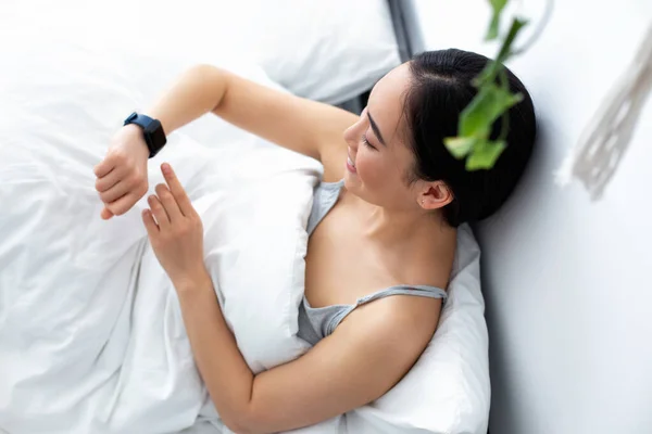 Mujer alegre con reloj inteligente en la cama —  Fotos de Stock