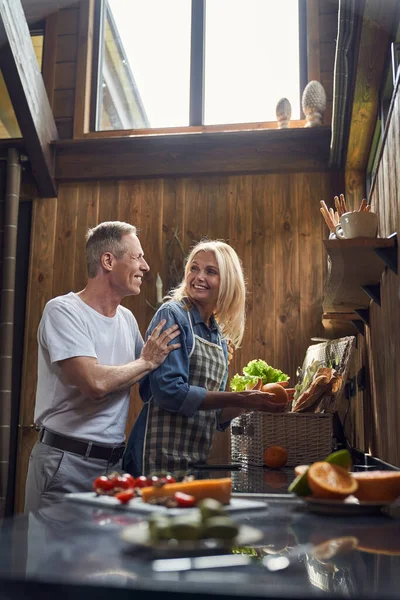 Vrolijke volwassen echtgenoten hebben plezier in houten keuken — Stockfoto