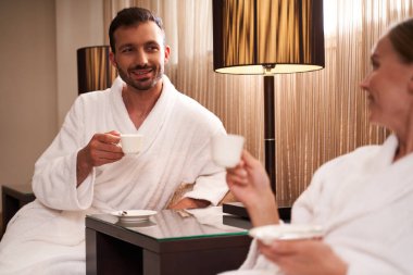 Bornozlu bir çiftin ellerinde kahve fincanları.