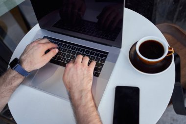 Akıllı telefonlu ve bilgisayarlı bir adam kahve içiyor.