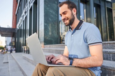 Şehir merkezinde dizüstü bilgisayarı olan mutlu sakallı adam.