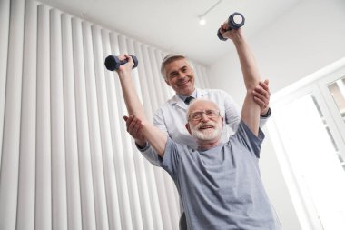 Neşeli kıdemli adam klinikte doktorla antrenman yapıyor.