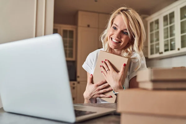 Positive woman putting box to her chest while hugging it — Stock Photo, Image