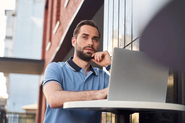 Un jeune homme confiant utilisant un ordinateur portable dans un café de rue — Photo