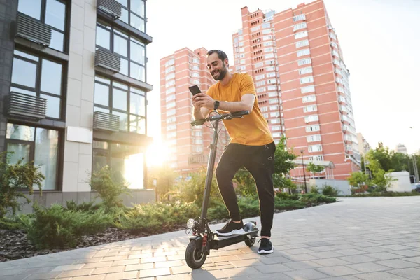 Vrolijke jongeman met smartphone paardrijden scooter — Stockfoto
