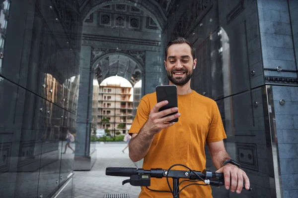 Glimlachende man met baard en smartphone rijden in stedelijke omgeving — Stockfoto