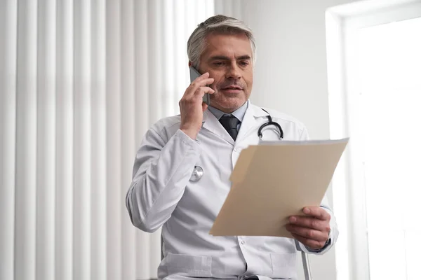 Érett orvos beszél okostelefonon a munkahelyen — Stock Fotó