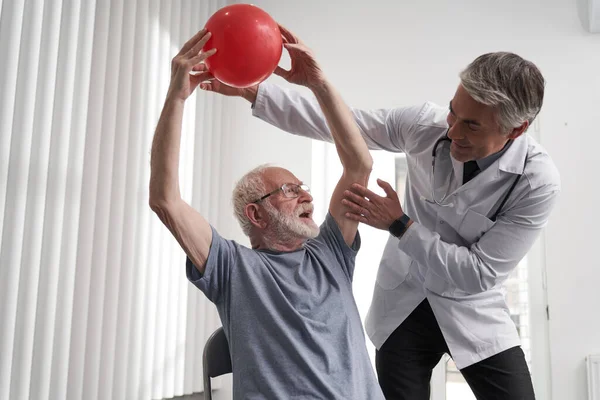 Deneyimli doktor yaşlı bir adamla fiziksel egzersiz yapıyor. — Stok fotoğraf