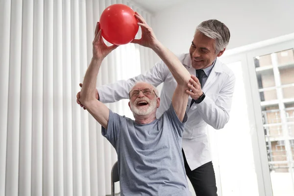 Mutlu yaşlı adam, doktor yardımıyla topu kaldırıyor. — Stok fotoğraf