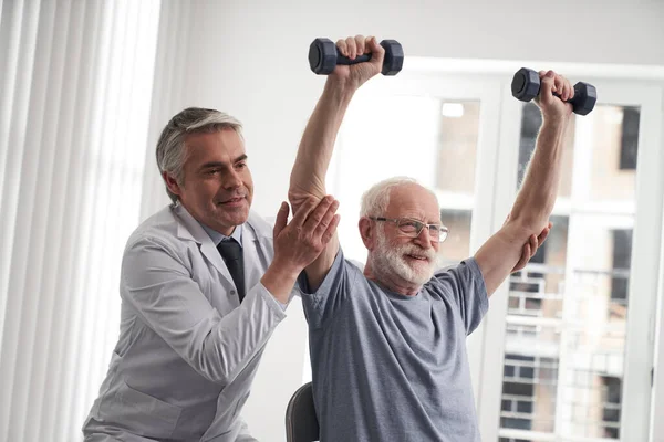 Lächelnder männlicher Rehabilitator hilft älteren Patienten beim Sport — Stockfoto