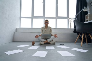 Sakin iş kadını evde dizüstü bilgisayarla meditasyon yapıyor.