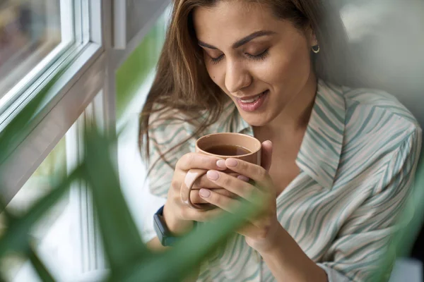 Щаслива жінка насолоджується чашкою кави в приміщенні — стокове фото
