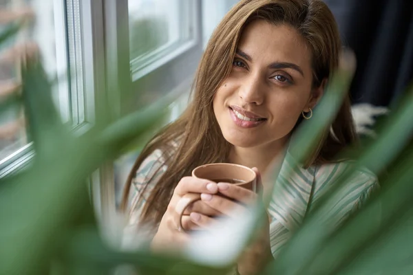 Senhora bonita alegre com xícara de bebida quente dentro de casa — Fotografia de Stock