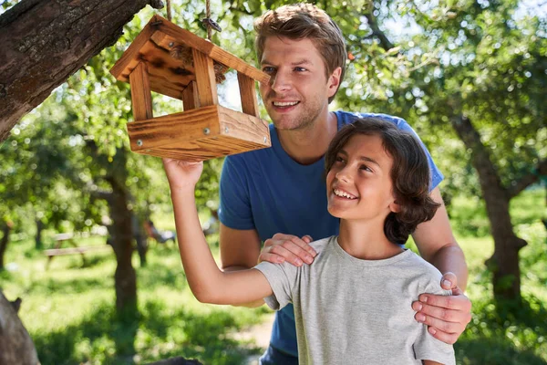 Щасливий батько і син вішають годівницю для птахів на дереві — стокове фото
