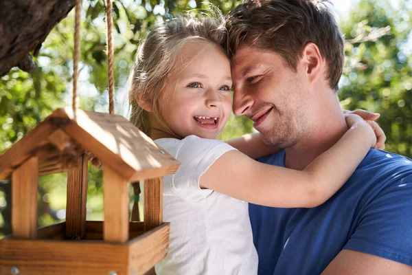 Alegre padre e hija abrazándose junto al árbol con comedero de aves — Foto de Stock