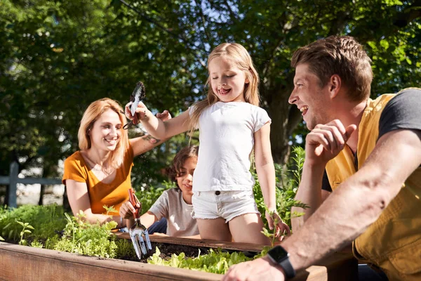 Cheerful kids planting flowers with parents in garden — Stock Photo, Image