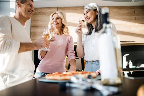 Szczęśliwy mężczyzna i dwie kobiety w kieliszkach do wina w kuchni — Zdjęcie stockowe