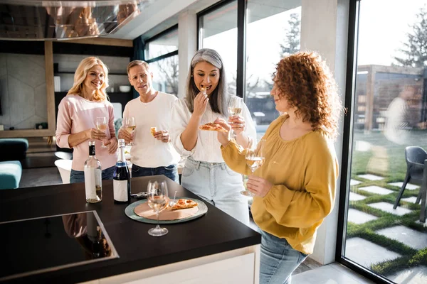 Két nő friss pizzát kóstol a konyhában. — Stock Fotó