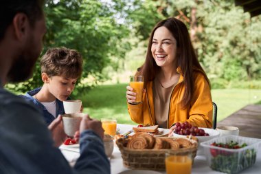 Neşeli genç bayan dışarıda ailesiyle kahvaltı yapıyor.
