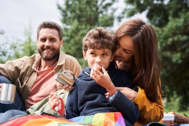 Sevgi dolu ebeveynler, sevimli oğullarıyla dışarıda piknik yapıyorlar.
