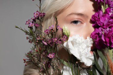 Çekici bir genç kadın yüzünü çiçeklerle örtüyor.