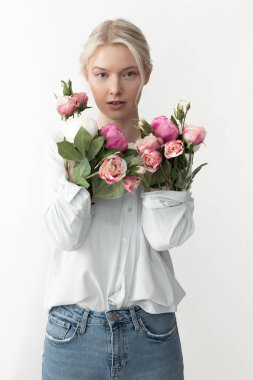 Kollarında çiçeklerle kollarını gösteren güzel genç bir kadın.