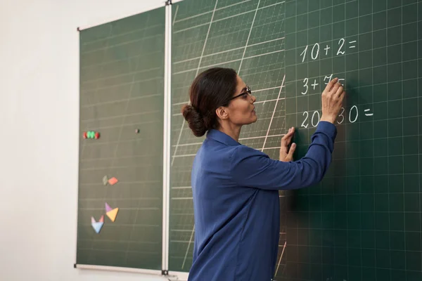 Profesora escribiendo en pizarra en sala de clase — Foto de Stock