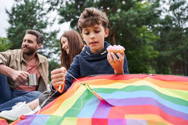 Очаровательный мальчик играет с воздушным змеем во время пикника с родителями — стоковое фото