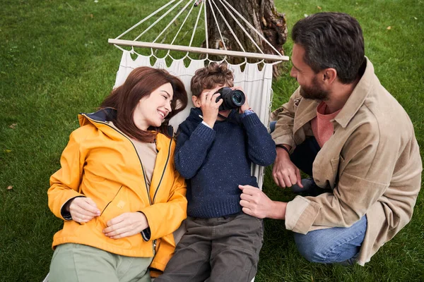 Male kid using camera while spending time with parents outdoors — Stock Photo, Image