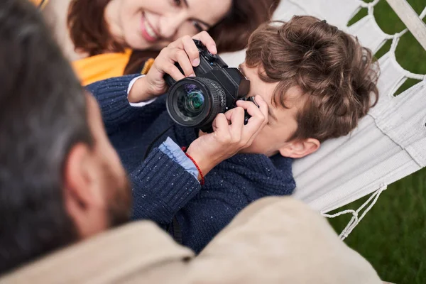 Chico de pelo rizado usando la cámara mientras pasa tiempo con los padres al aire libre — Foto de Stock