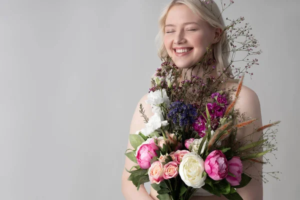 Joyful young woman with flowers standing against gray background