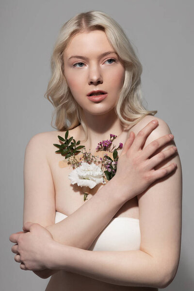 Очаровательная женщина с растениями на коже, стоящими на сером фоне