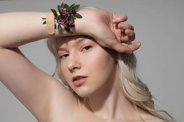 Charmante jonge vrouw met bloemen op haar hand staan tegen grijze achtergrond — Stockfoto