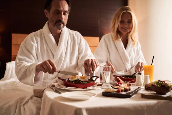 Calma pareja disfrutando de la comida en la cama en la habitación del hotel —  Fotos de Stock