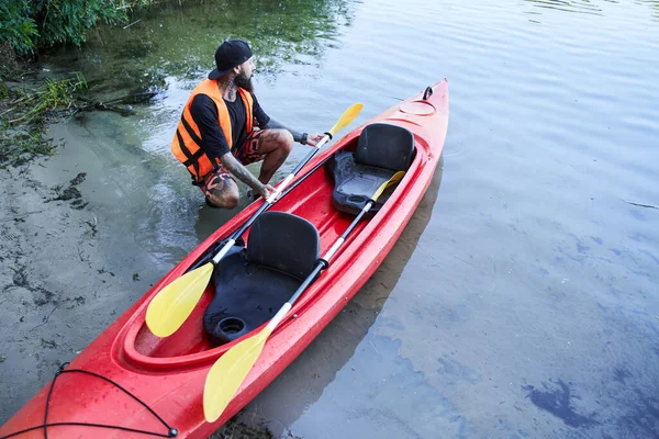 Menutup pria ditembak duduk di dekat kano di pantai berpasir — Stok Foto