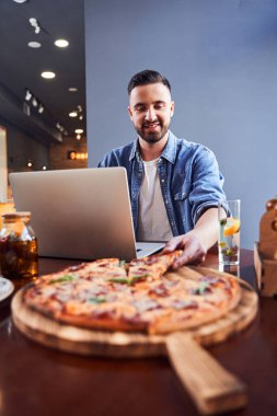 Bilgisayarlı bir adam iş yerinde pizza yiyor.