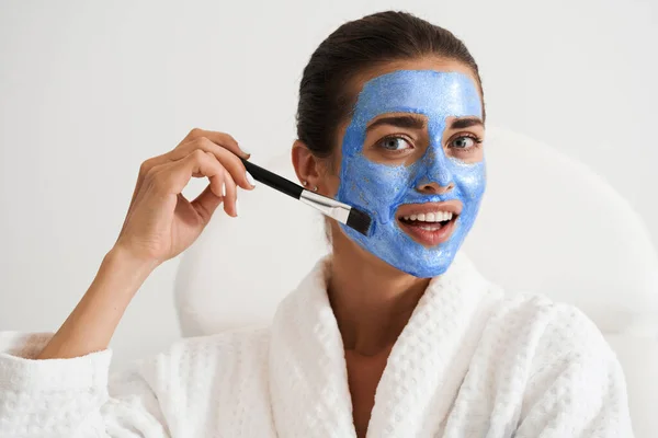 Gadis menerapkan masker tanah liat biru wajah — Stok Foto