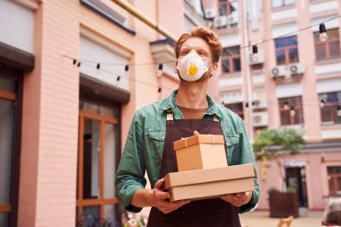 Maskeli bir adam hediye kutuları tutuyor.