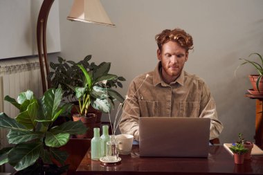 Masada dizüstü bilgisayarı olan kızıl saçlı işçi oturuyor.