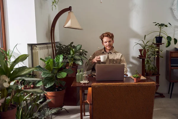 Werknemer met laptop aan tafel en het drinken van koffie — Stockfoto