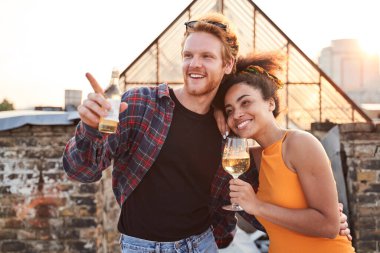 Neşeli genç aşıklar şehir çatısında sarılıyorlar.