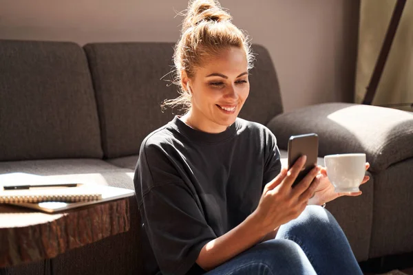 Elégedett hölgy mosolyog használata közben az okostelefon otthon — Stock Fotó