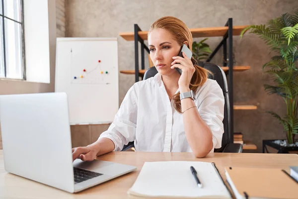 Mujer seria trabajando y hablando por teléfono — Foto de Stock