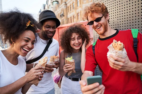 O companie tânără fericită cu smartphone-uri și hot dog — Fotografie, imagine de stoc